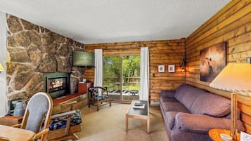 A cozy living room with a stone wall, a fireplace, a television, and a view of the outdoors.