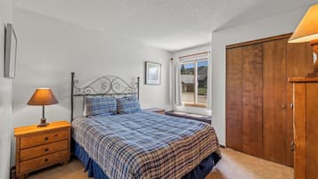 Une chambre à coucher comprenant un lit, une table de chevet, une armoire en bois, une fenêtre donnant sur un paysage agréable et un tableau encadré accroché au mur.