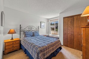 Une chambre à coucher comprenant un lit, une table de chevet, une armoire en bois, une fenêtre donnant sur un paysage agréable et un tableau encadré accroché au mur.
