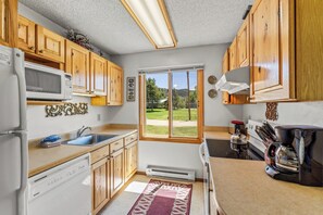 Une cuisine avec des meubles en bois, un four à micro-ondes, un évier, une cuisinière et une fenêtre donnant sur un paysage verdoyant.