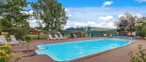 Uma piscina com deck de madeira, cadeiras de descanso e área cercada com boia salva-vidas.