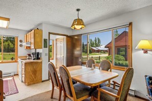 Un coin repas avec une table et des chaises en bois, une cuisine avec des meubles en bois et une vue sur un immeuble par de grandes fenêtres.