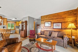 A cozy living room with a sofa, armchair, and coffee table, a kitchen with wooden cabinets, and a dining area with a table and chairs.