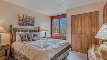 A bedroom with a large bed, wooden headboard, a window with a view, a wooden wardrobe, and a painting on the wall.