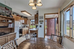Una cocina amplia con armarios de madera, una mesa de comedor y sillas. Hay un refrigerador, un microondas y un lavaplatos. La cocina tiene un ventanal y una puerta que da a un patio.