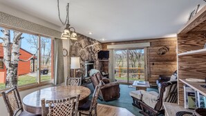 A cozy interior with a stone wall, wooden furniture, and large windows offering a view of the outdoors. - Grizzly - Stunning mountain views on the Elk River (Clark)