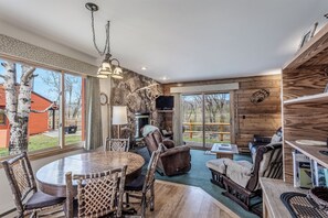 A cozy interior with a stone wall, wooden furniture, and large windows offering a view of the outdoors.