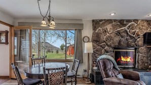 A cozy living room with a stone fireplace, a dining table with chairs, and a view of the outdoors. - Grizzly - Stunning mountain views on the Elk River (Clark)