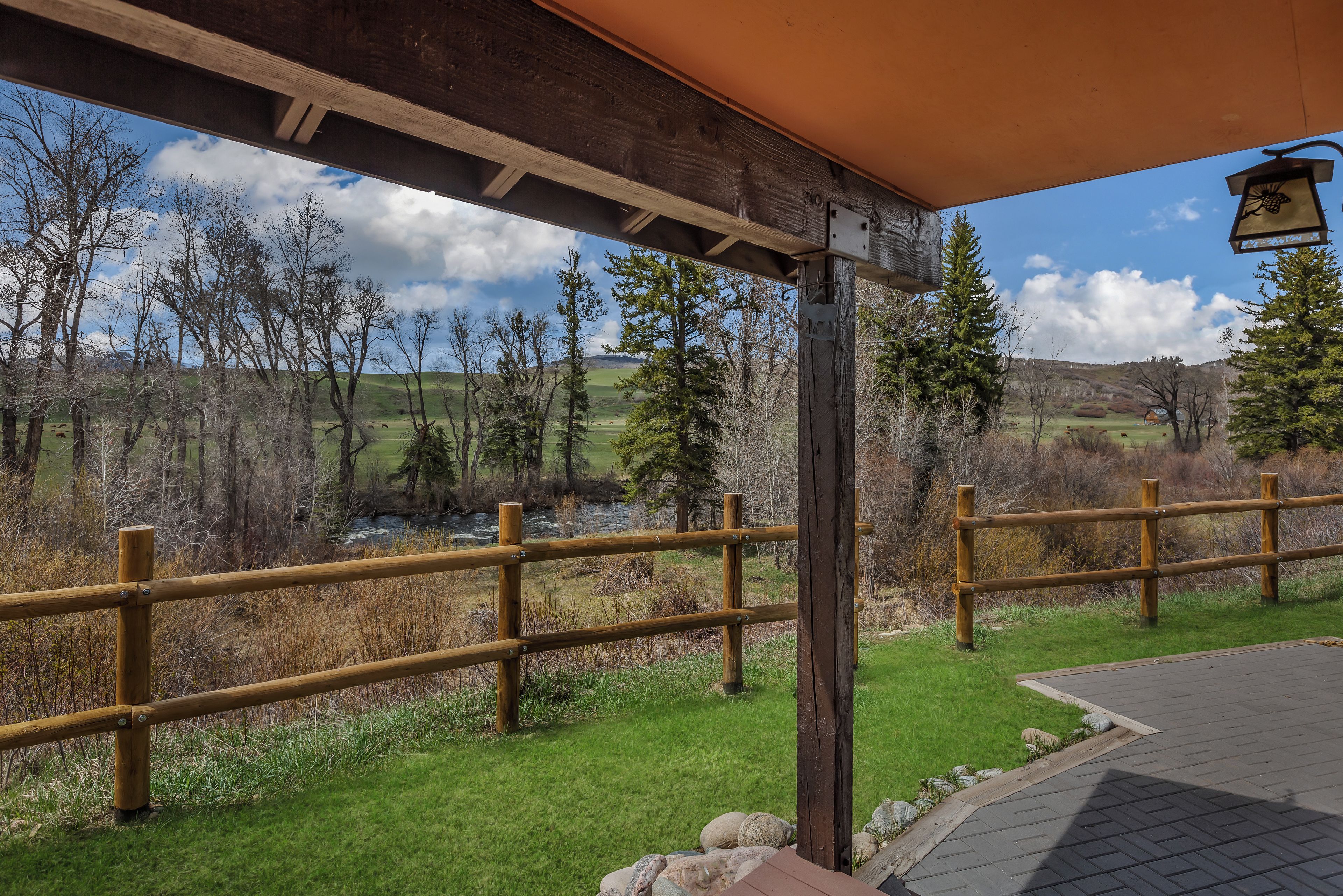 A covered outdoor area with a wooden fence, a stone wall, and a view of a river and trees.