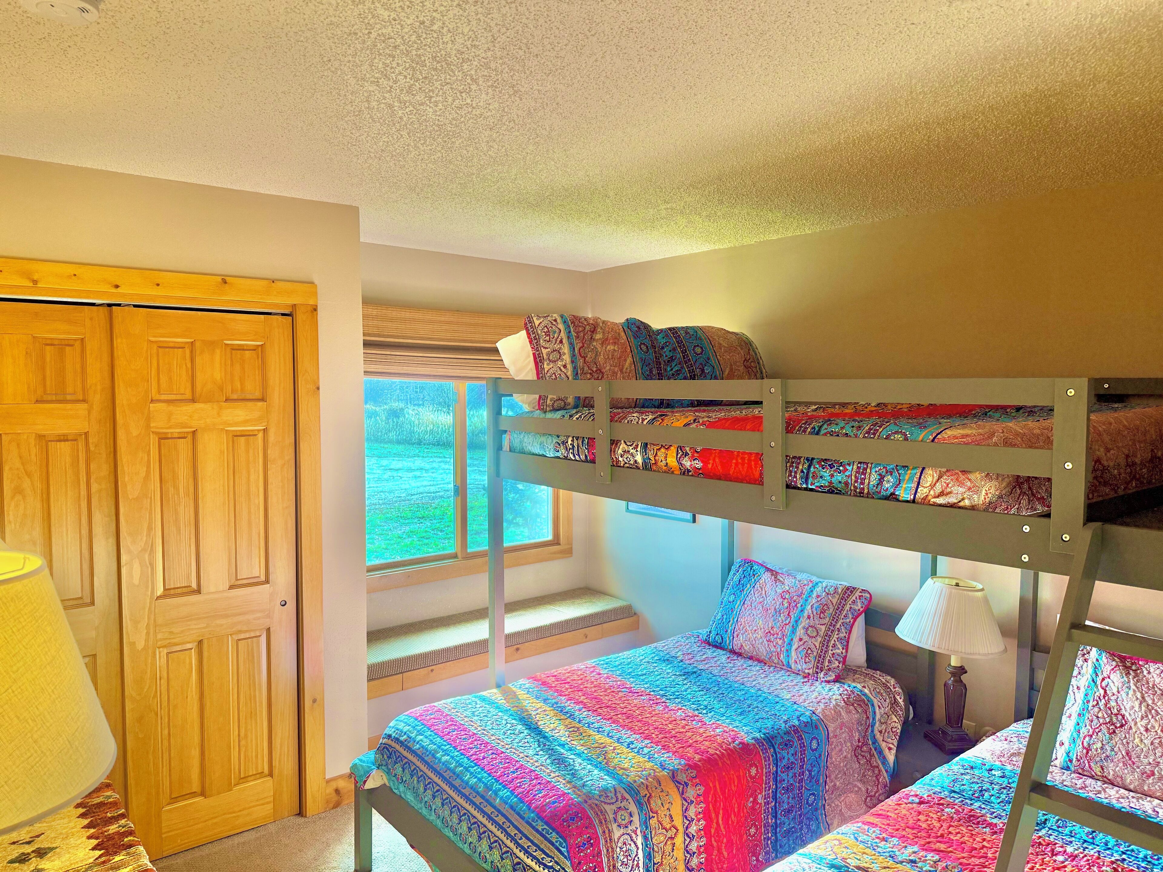 A bunk bed room with a window, a wooden door, and a lamp.
