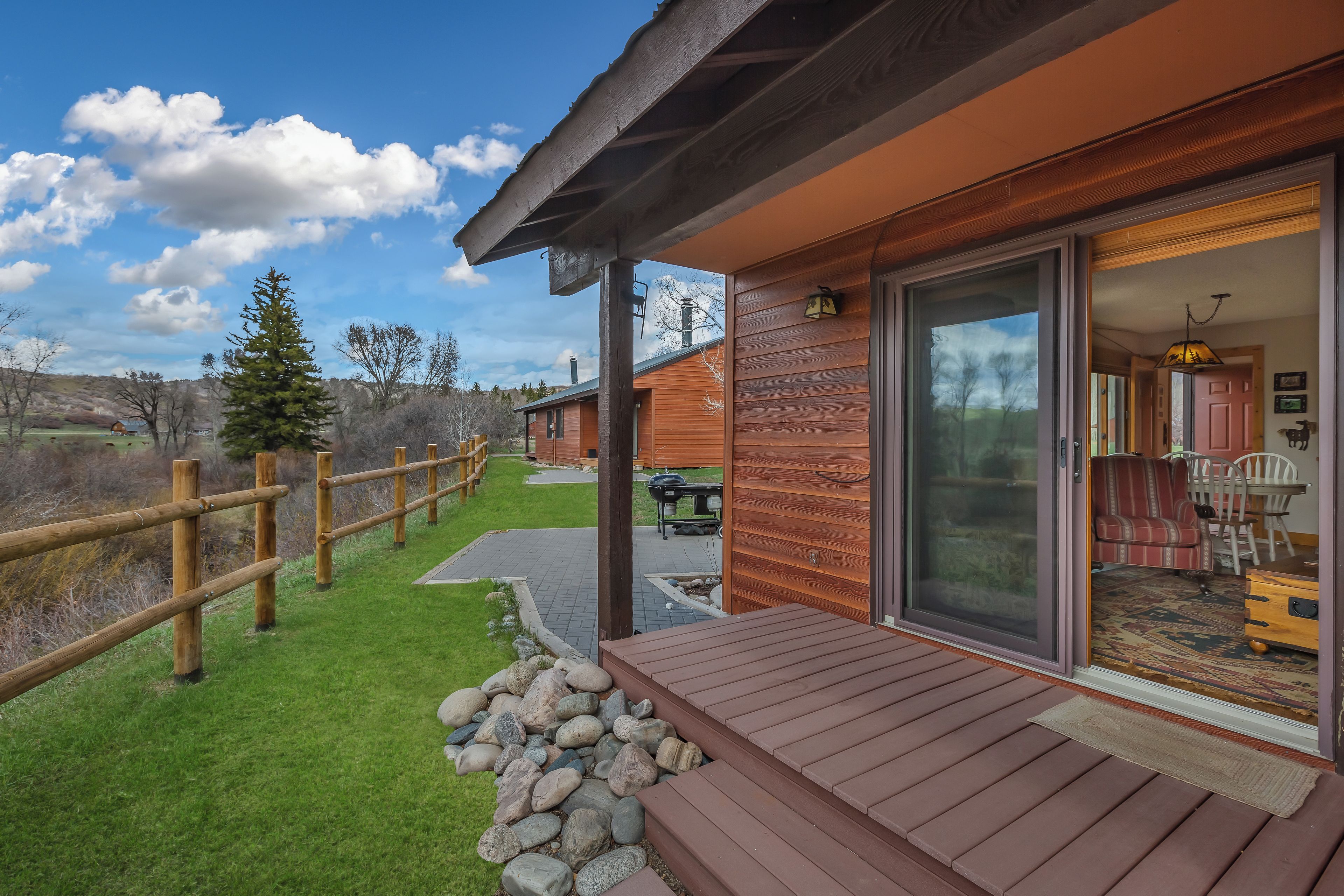 A wooden cabin with a covered deck, a sliding glass door leading to an interior with a dining area and a fireplace.