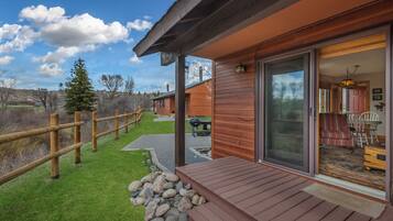 A wooden cabin with a covered deck, a sliding glass door leading to an interior with a dining area and a fireplace.