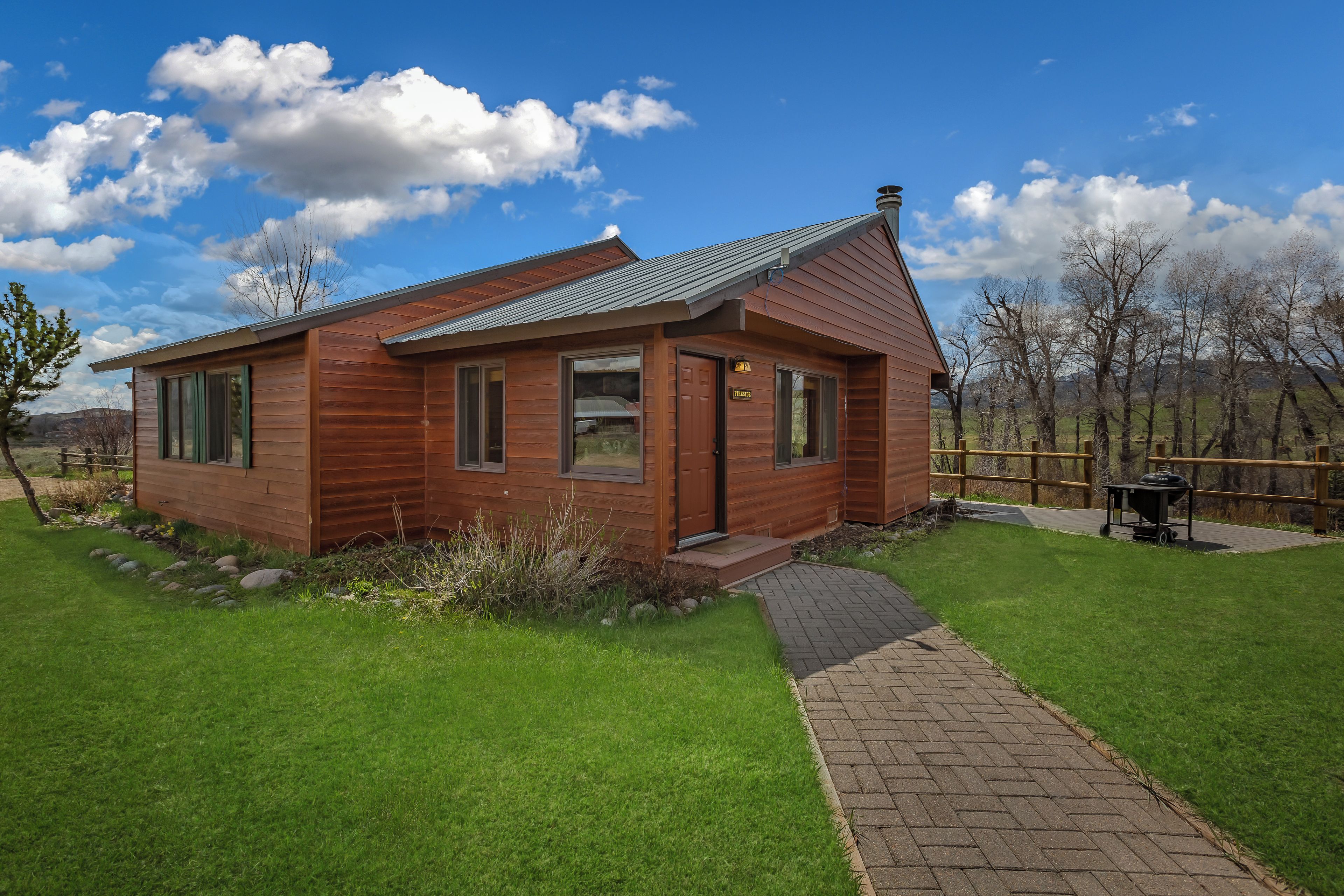 Une cabane en bois avec un toit en métal, une allée pavée et une cour gazonnée.