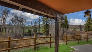 A covered outdoor area with a wooden fence, a stone wall, and a view of a river and trees. - Fireside - Quaint cabin near hiking and fishing (Clark)