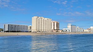 A beachfront hotel with multiple floors, a sandy beach, and a clear blue sky.