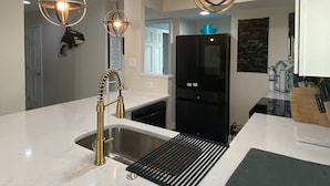 A modern kitchen with a stainless steel sink, a black refrigerator, and two pendant lights with exposed bulbs.