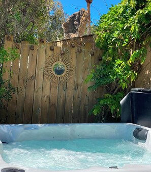 Un jacuzzi en un patio trasero con valla de madera y un espejo decorativo.