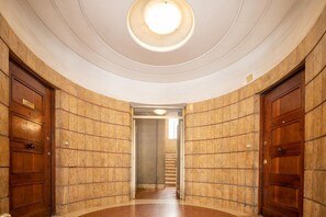 A hallway with a circular skylight, wooden doors, and a staircase in the background. - Sweeties apartment san Giovanni (Roma)