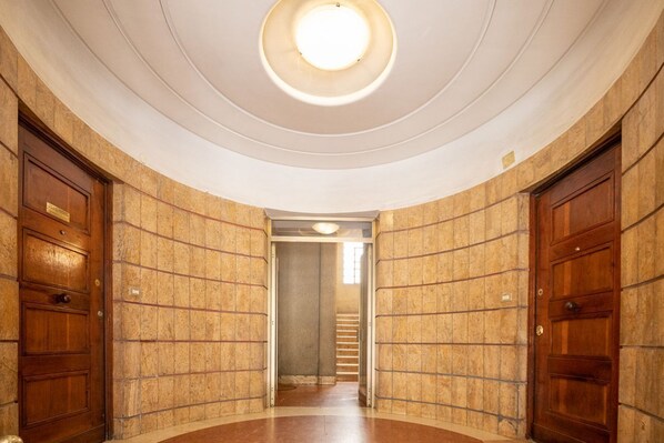 A hallway with a circular skylight, wooden doors, and a staircase in the background. - Sweeties apartment san Giovanni (Roma)