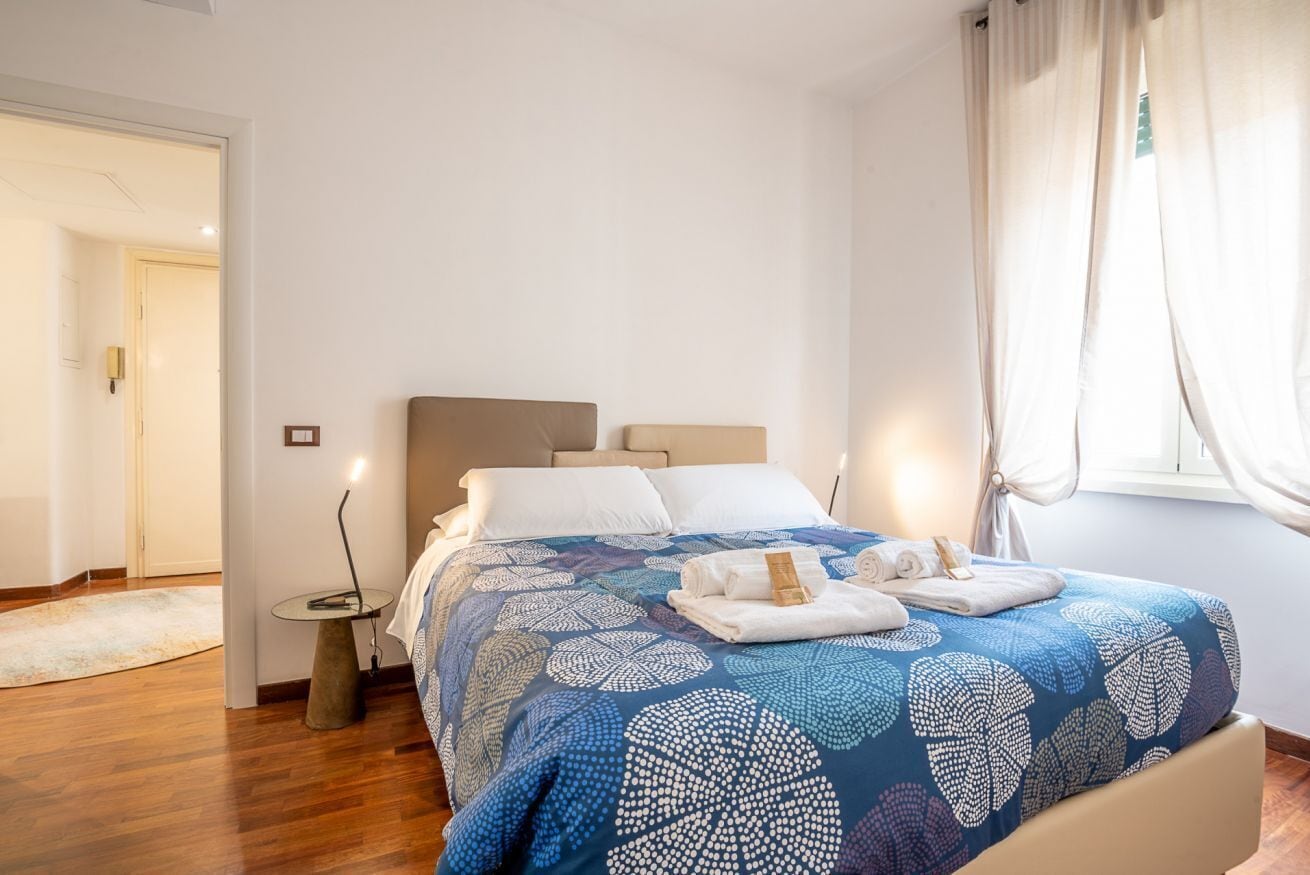 A bedroom with a bed, bedside table, and a window with curtains.