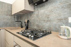 A modern kitchen with a gas stove, a kettle, and a backsplash of grey tiles. - Sweeties apartment san Giovanni (Roma)