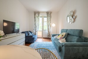 A room with a bed, a TV, a blue sofa, a chair, and a window with curtains.