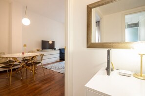 A modern room with a round dining table, chairs, a flat-screen TV, a large mirror, and a bedside table with a lamp and a device. - Sweeties apartment san Giovanni (Roma)