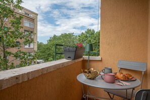 Un balcon avec une table, une chaise, des plantes en pot et un bâtiment en arrière-plan.