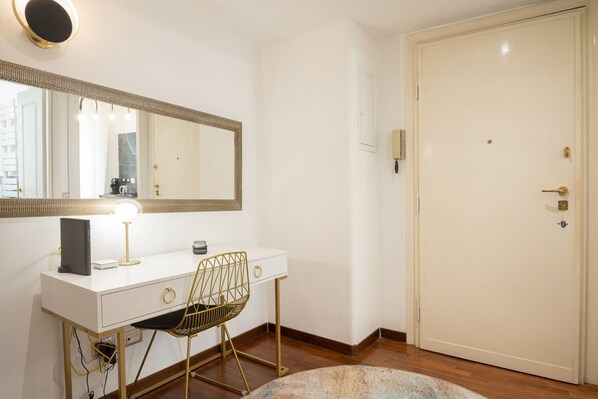 A white desk with a computer, a lamp, and a chair in a room with a door and a mirror.