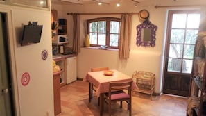 A compact kitchen with a dining area, a small refrigerator, a microwave, and a window with curtains.