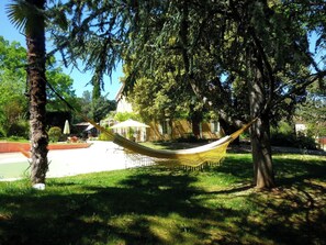 A hammock under a tree in a park with a building in the background.