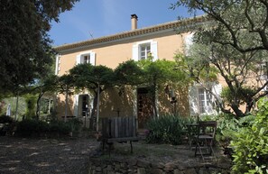 A building with a stone wall, a wooden bench, and a table with chairs in the foreground.