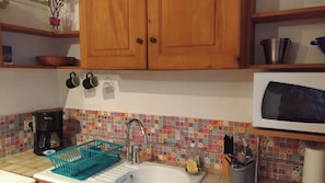 A kitchen with wooden cabinets, a tiled backsplash, a coffee maker, a sink, and a microwave.