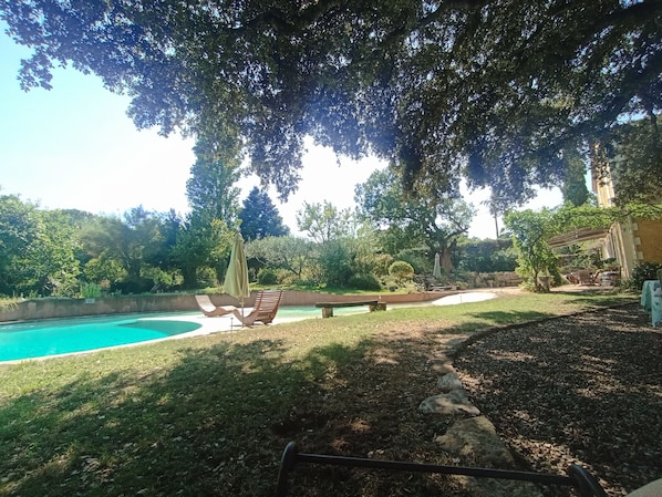 A swimming pool with lounge chairs and a bench, surrounded by trees and a stone wall.