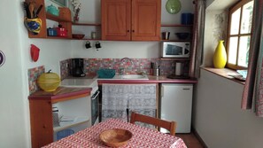 Cuina compacta amb armaris de fusta, microones, rentapelats i taula de dinar amb mantell estampat.