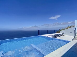 A swimming pool with a view of the ocean, lounge chairs, and a modern building.