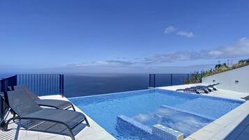 Una piscina infinita moderna con vistas despejadas al océano, acompañada de sillones de descanso y un pequeño jacuzzi.