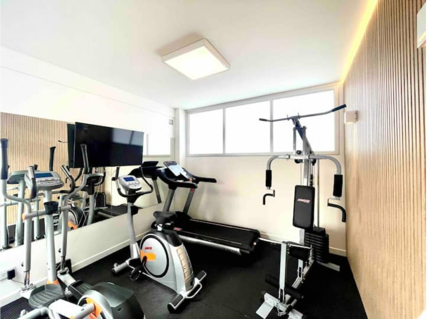 A gym with cardio machines, weight equipment, and a TV screen.