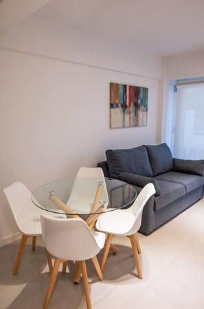 En moderne stue med et glasbord, hvide stole og en grå sofa.