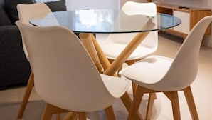 Una sala de estar moderna con una mesa de comedor de vidrio, sillas blancas, un sofá gris y un televisor de pantalla plana montado en la pared.