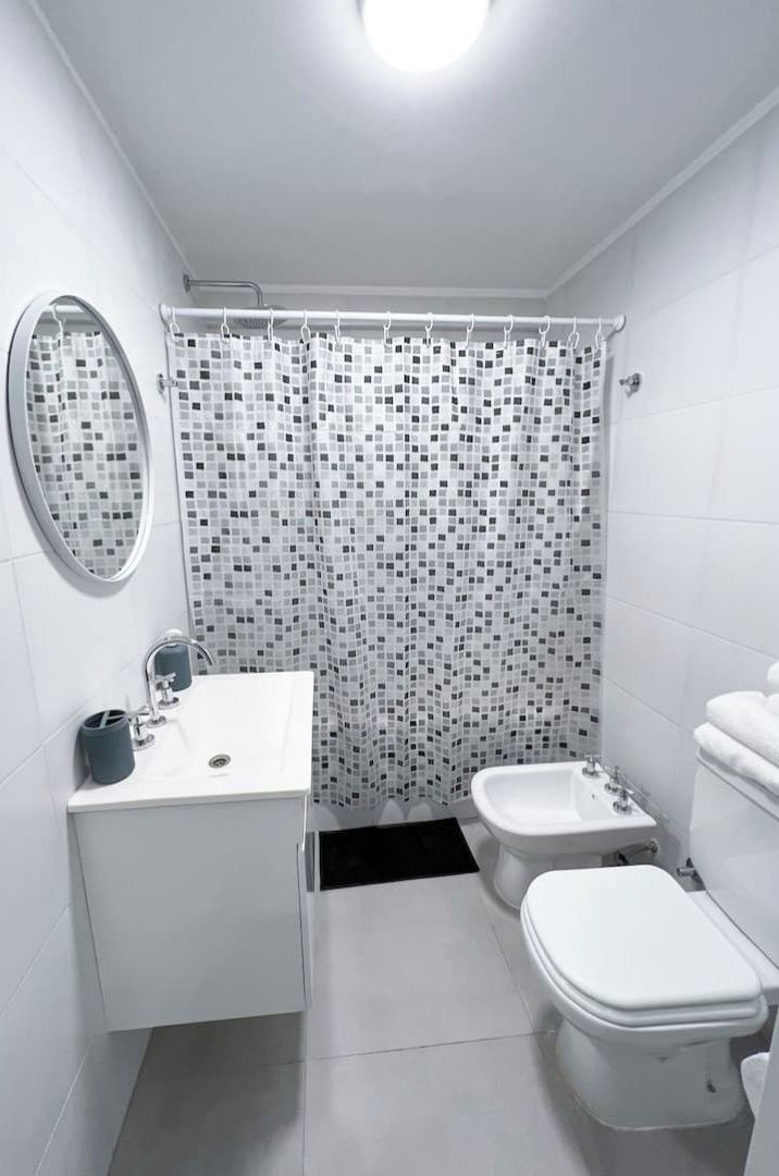 Un baño moderno con un lavamanos blanco, un bidé, un inodoro y una cortina de ducha con un diseño de mosaico.