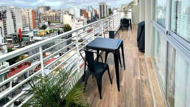 Un balcón con mesa y sillas, con vistas a un paisaje urbano con varios edificios.