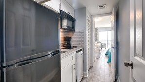 A narrow kitchen with a stainless steel refrigerator, a microwave, and a dishwasher. - Myrtle Beach Condo w/ Ocean View + Pool Access! (Myrtle Beach)