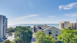 A coastal residential area with modern buildings, a clear sky, and a view of the ocean. - Myrtle Beach Condo w/ Ocean View + Pool Access! (Myrtle Beach)
