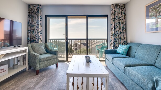 A modern living room with a sofa, armchair, and TV on a white console table. - Myrtle Beach Condo w/ Ocean View + Pool Access! (Myrtle Beach)