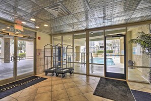 A hotel lobby with a glass door entrance, a pool visible through the door, and a metal cart near the entrance.