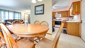 Un coin repas avec une table et des chaises en bois, une cuisine avec des meubles et des appareils électroménagers en bois, et un salon avec un canapé et des rideaux.