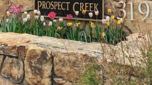 A stone wall with a sign reading "OUTLAWS 323" and "PROSPECT CREEK 319" surrounded by flowers.