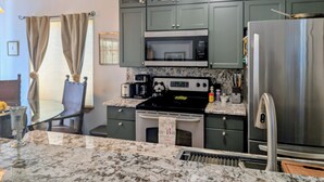 A kitchen with green cabinets, a stainless steel refrigerator, a microwave, a stove, and a sink.