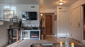 A living room with a flat-screen TV, a fireplace, a bookshelf, and a coffee table with candles.